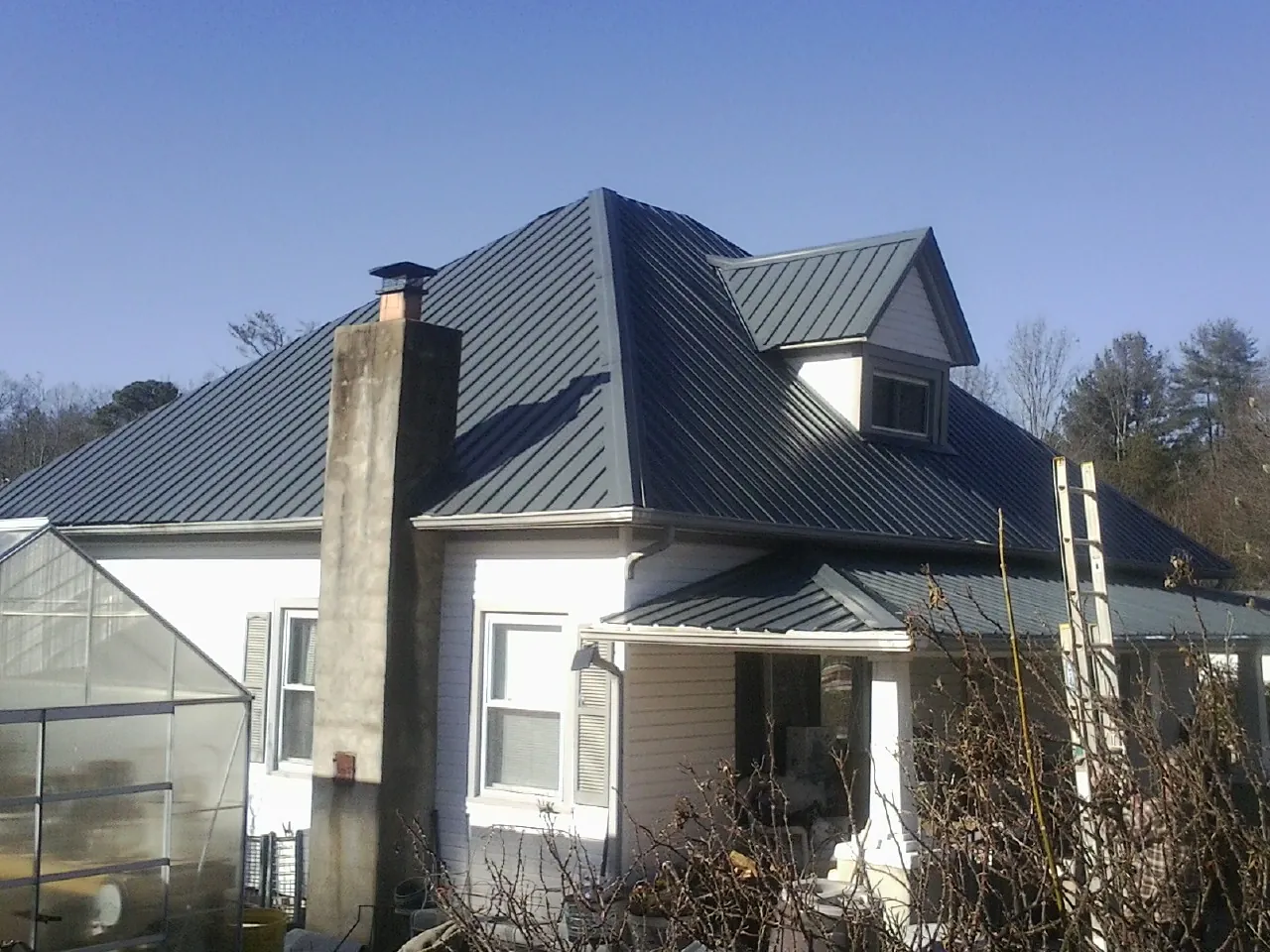 Dark blue standing seam metal roof on a white farmhouse with dormer — Slate & Tile Roof Repair by Roofing Brothers in Clarkdale