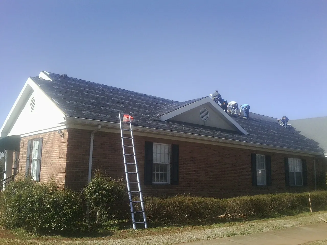 Crew tearing shingles off a brick ranch roof with a ladder set — Metal Roof Repair work by our crew in Clarkdale