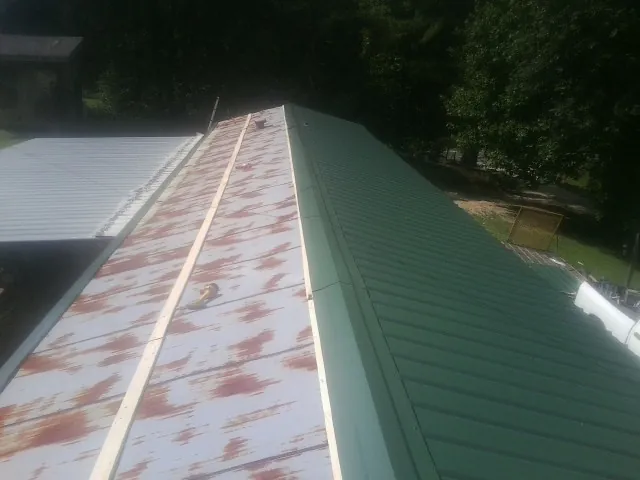 Old rusted panels beside newly installed green metal roofing — Wind Damage Roof Repair by Roofing Brothers in Clarkdale