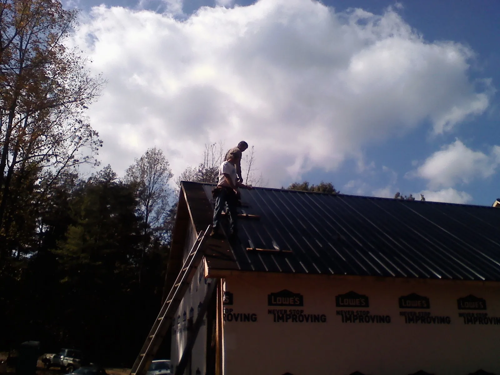 Roofer fastening dark metal panels high against a cloudy sky, from a Roof Inspection job in Clarkdale
