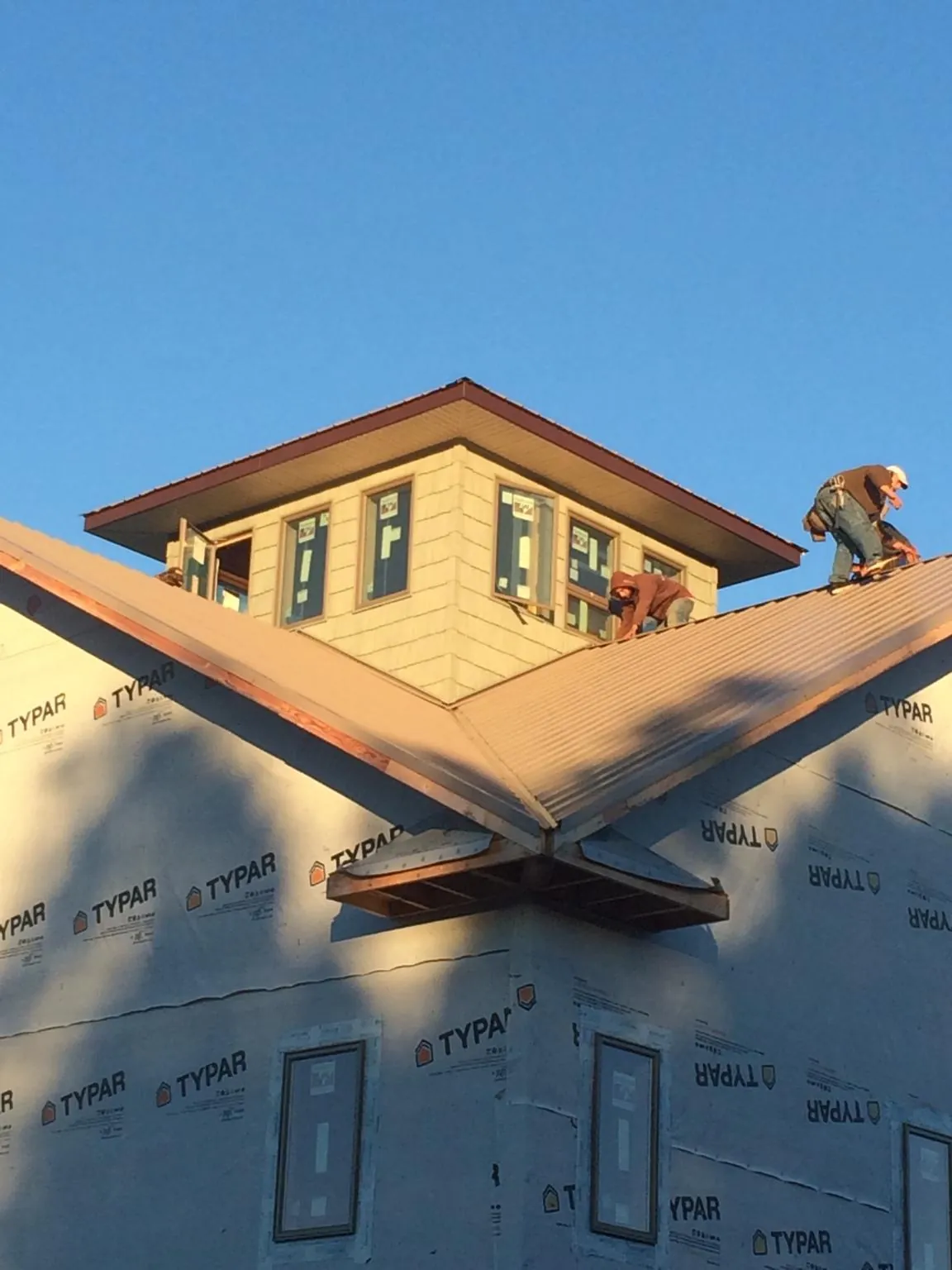 Roofers working around a rooftop cupola on a new metal roof at sunset — Roof Waterproofing in Clarkdale by Roofing Brothers